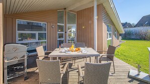 A covered outdoor patio with a table set for dining, wicker chairs, and a barbecue grill.