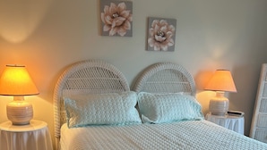Une chambre à coucher avec un grand lit, deux tables de chevet avec des lampes et deux tableaux représentant des fleurs, accrochés au mur.