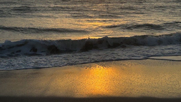 Une plage où le soleil se couche sur l’océan, et où les vagues viennent doucement se briser sur le rivage.