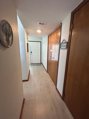 A hallway with wooden flooring, a white door at the end, and a wooden door on the right. - Ocean view, North facing, bldg is beachfront, near restaurants, attractions. (Cocoa Beach)