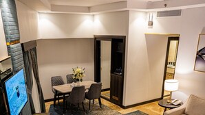 A hotel room with a dining area, a sofa, a TV, and a desk with a computer and papers. - ODST Jed (Jeddah)