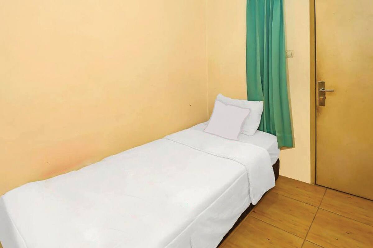 A single bed in a room with a plain yellow wall and a green curtain.