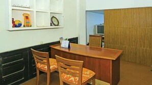 A small dining area with a wooden table and two chairs, a shelf with toys and a clock, and a wooden partition in the background. - Backpacker Homestay Cibubur by PEKOTEL (Bekasi)