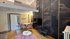 A modern living room with a loft area, a dining table with chairs, a pink rug, and a TV on a stand. - Chic Turin house in the historic center (Torino)