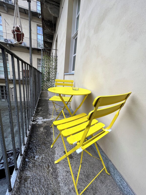 A balcony with yellow metal chairs and tables, a hanging plant, and a metal railing.