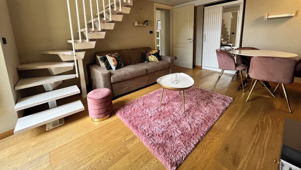 A modern living room with a staircase, a sofa, a pink rug, and a dining area. - Chic Turin house in the historic center (Torino)
