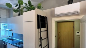 A compact kitchen with white cabinets, a black sink, and a small stove. There is a black ladder leaning against the wall and a potted plant on top of the cabinets. - Chic Turin house in the historic center (Torino)
