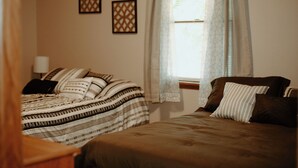 A bedroom with two beds, a window with sheer curtains, and two wall-mounted decorative items. - Charlotte's Cove - Right in the Heart of Amish Country (Millersburg)