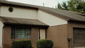A two-story house with a brick facade, a garage, and a small front yard with two bushes. - Charlotte's Cove - Right in the Heart of Amish Country (Millersburg)