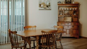 A dining area with a wooden table and chairs, a window with blinds, and a wooden cabinet with dishes. - Charlotte's Cove - Right in the Heart of Amish Country (Millersburg)