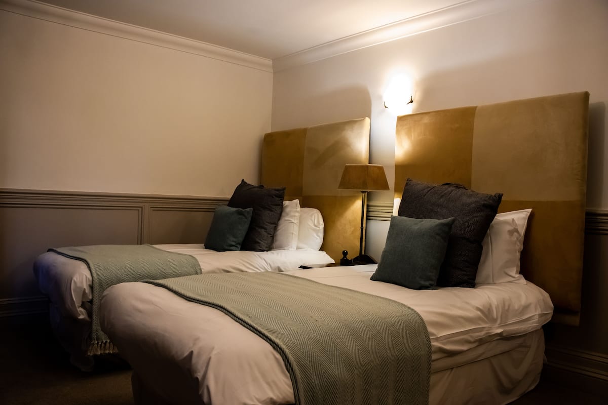 Een hotelkamer met twee bedden, een nachtkastje, een lamp en een wandlamp.