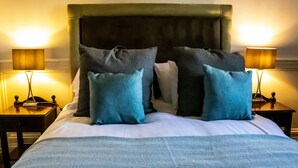 Un lit bien fait, recouvert d’une couverture bleue et agrémenté de plusieurs oreillers, avec deux tables de chevet de chaque côté, sur lesquelles sont posées des lampes.