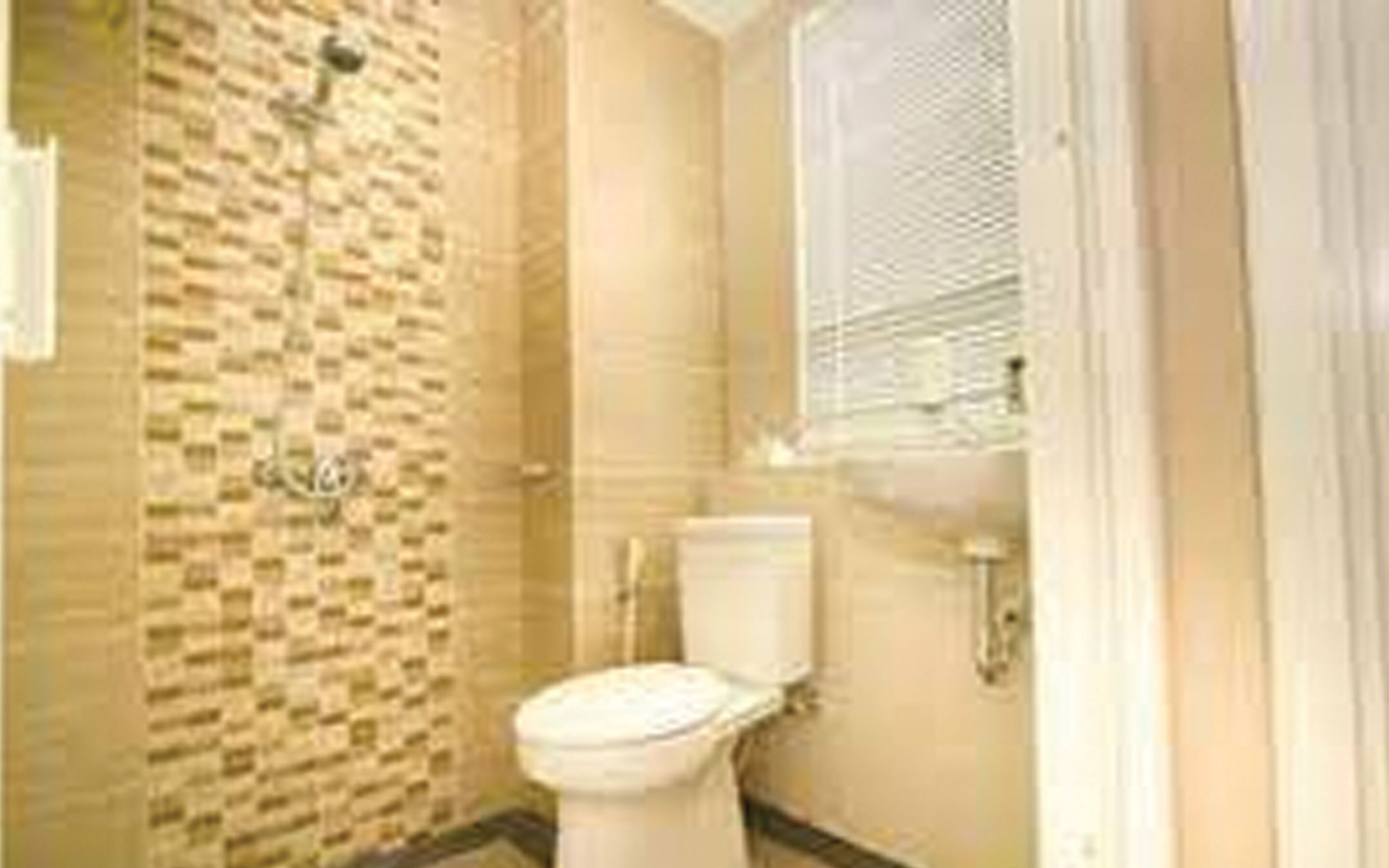 A bathroom with a tiled shower wall, a toilet, and a window with blinds.