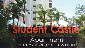 A sign for "Student Castle Apartment" with a backdrop of multi-story buildings and palm trees. - Student Castel By PEKOTEL (Depok)