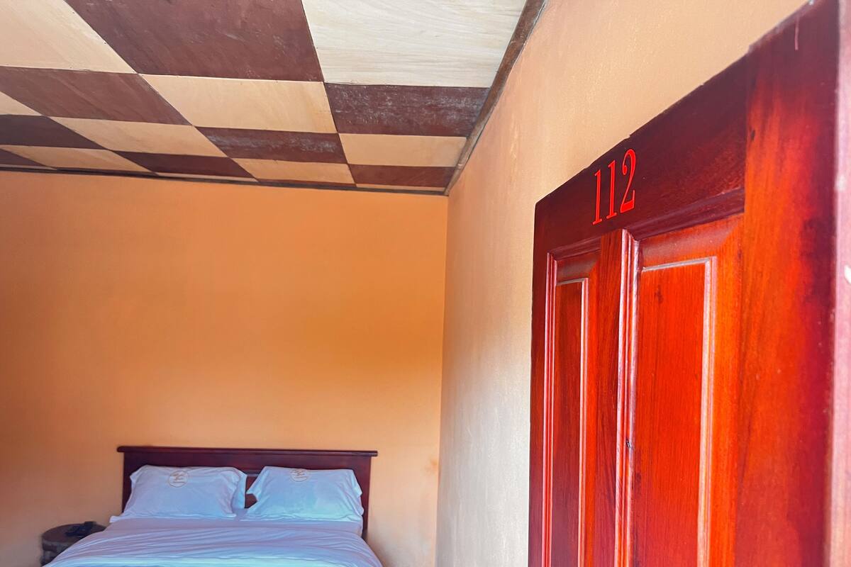 Une chambre d’hôtel avec un lit, une table de chevet et une porte portant le numéro 112.