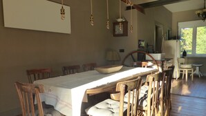 Un espace repas avec une longue table en bois, plusieurs chaises et des luminaires suspendus.