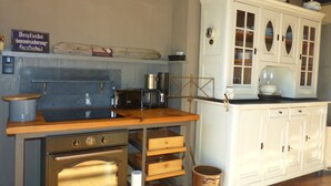 Une cuisine d’époque avec un plan de travail en bois, une cuisinière, une machine à café et un meuble blanc aux portes en verre.
