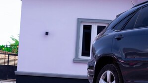 Um carro escuro estacionado em frente a um prédio com fachada rosa e moldura de janela branca.