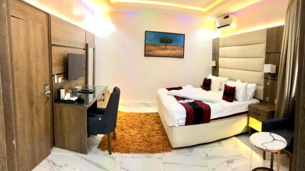 Quarto de hotel moderno com cama, escrivaninha e cadeira, um quadro na parede e luminária no teto.