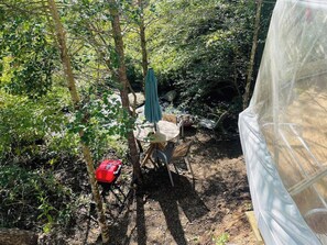 Un espacio al aire libre con mesas y sillas, rodeado de árboles y una estructura cubierta.