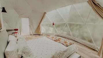 A tent-style room with a bed, a red chair, and a window with curtains.