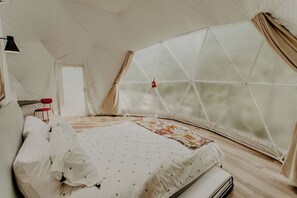 A tent-style room with a bed, a red chair, and a window with curtains. - Whispering Waters: Dome Getaway (Cosby)