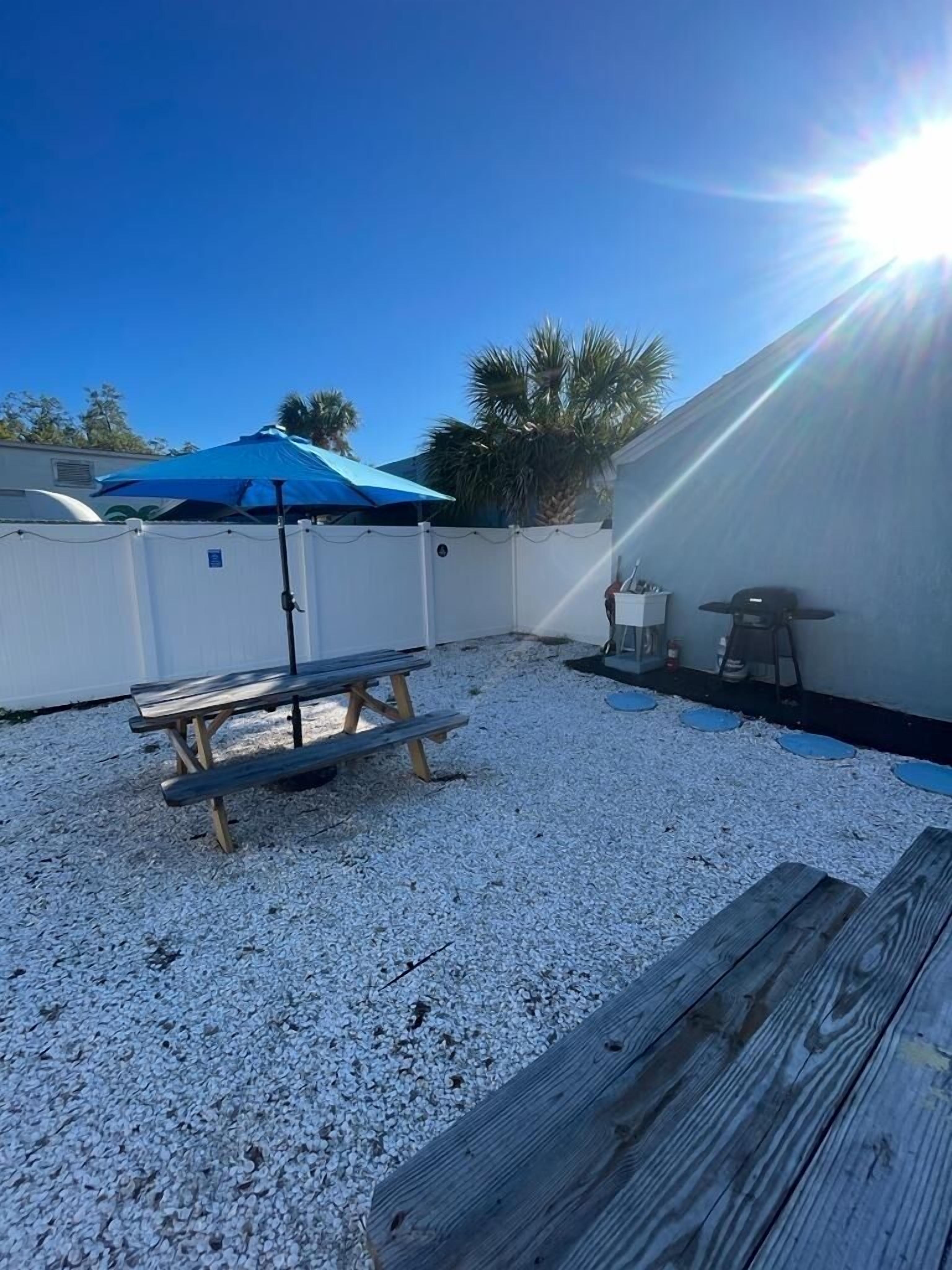 A backyard with a picnic table, a barbecue grill, and a blue umbrella.