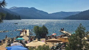A lakeside beach with people swimming and sunbathing, surrounded by mountains.