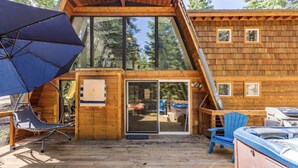 A wooden cabin with a deck, a hot tub, and a covered seating area.
