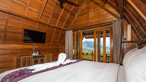 Ein Holzhütten-Zimmer mit Bett, Flachbildfernseher und Bergblick durch eine Glastür.