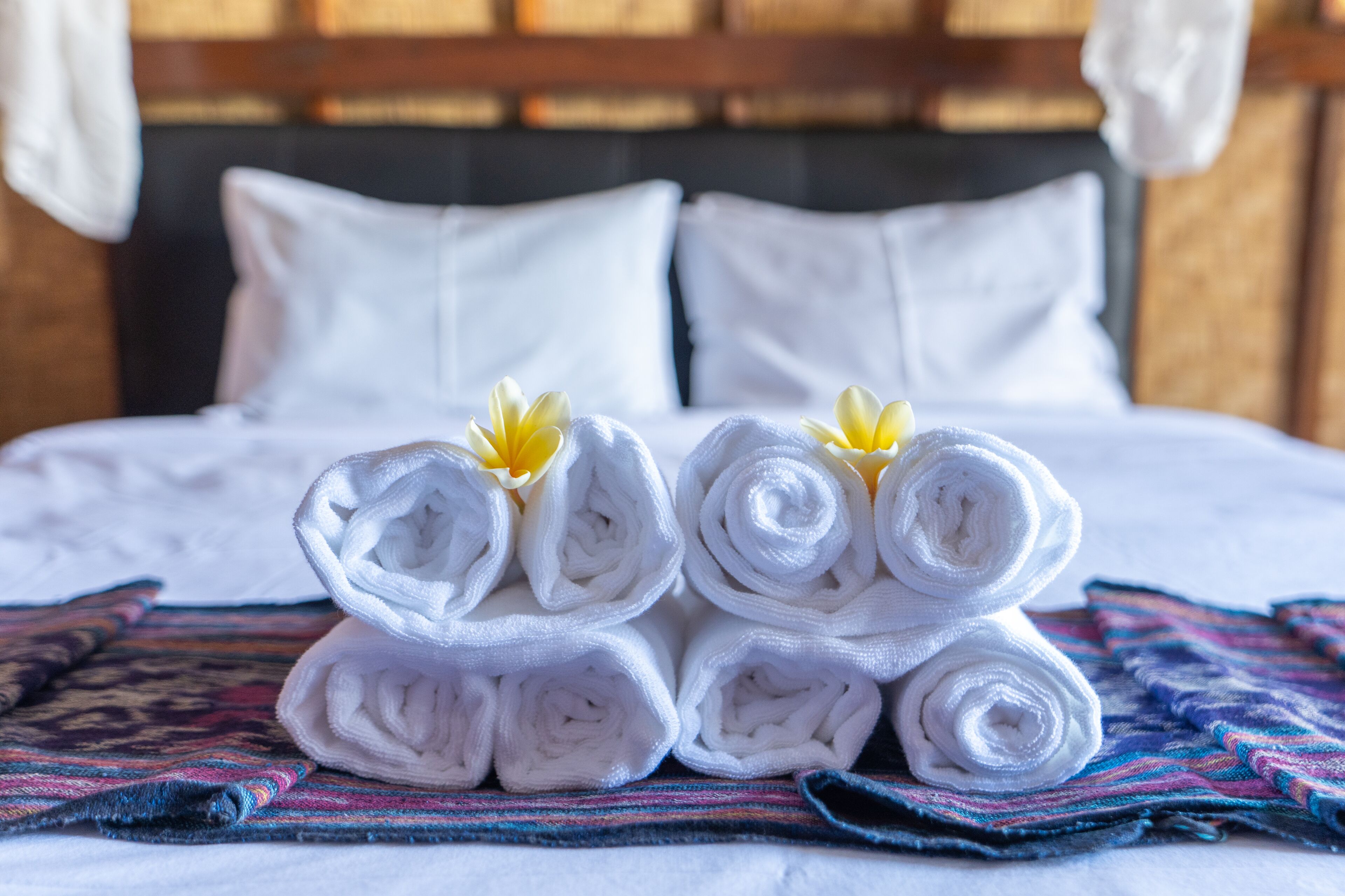 A neatly made bed with white linens and rolled towels, a colorful striped blanket, and a wooden headboard.