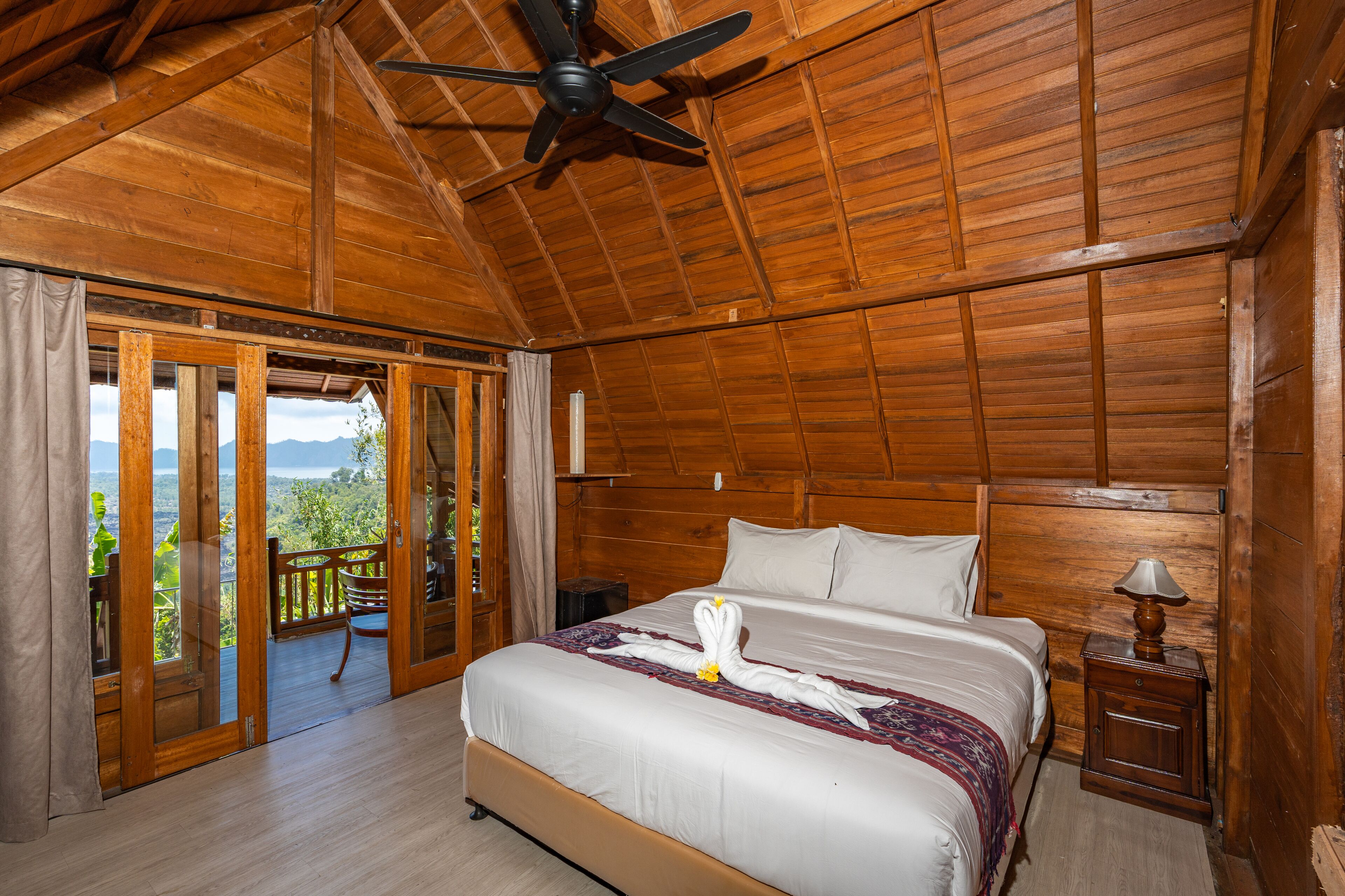A wooden-paneled bedroom with a bed, a ceiling fan, and a view through a glass door.