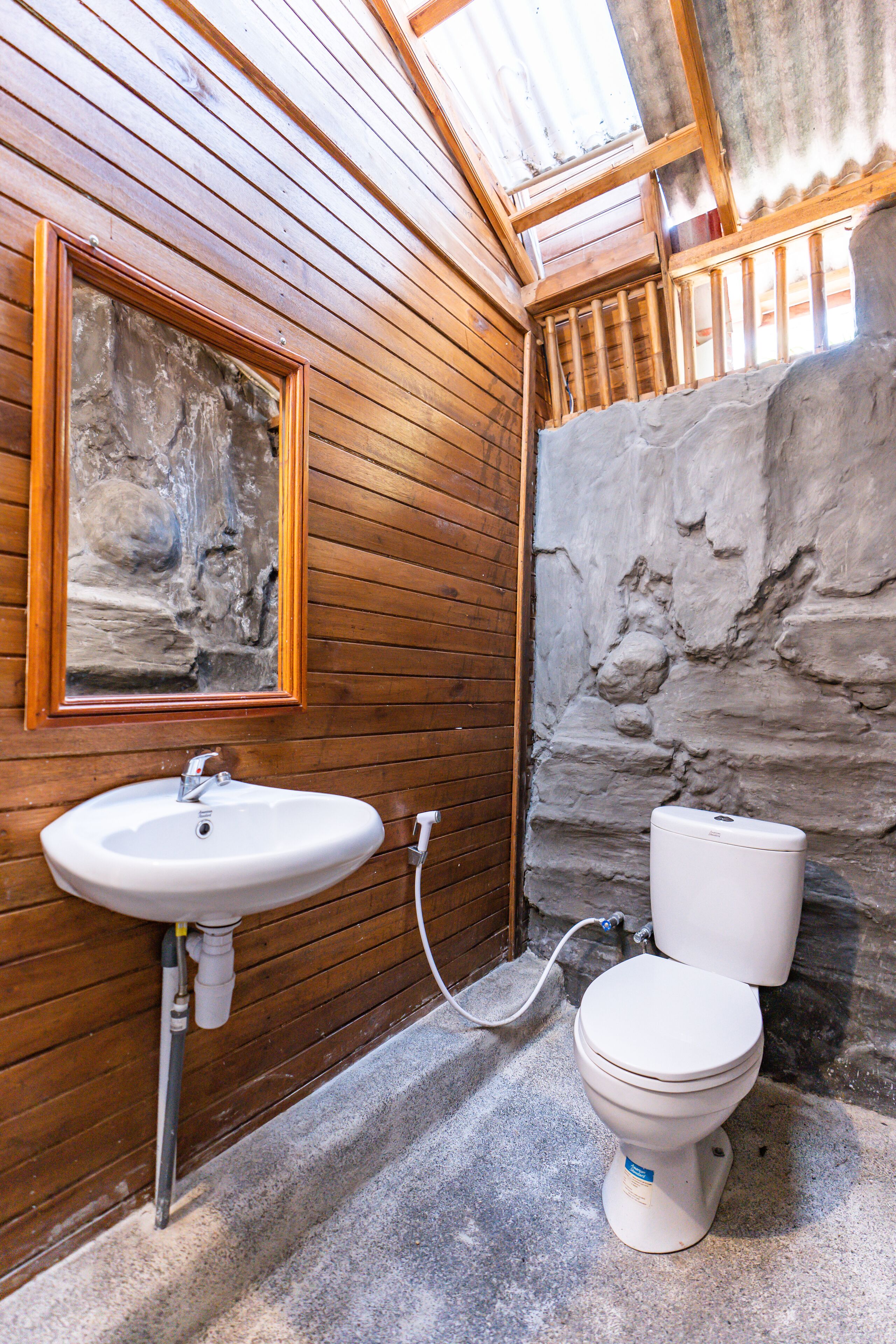 Un baño con paredes de madera, una pared de acento de piedra, un lavamanos y un inodoro.