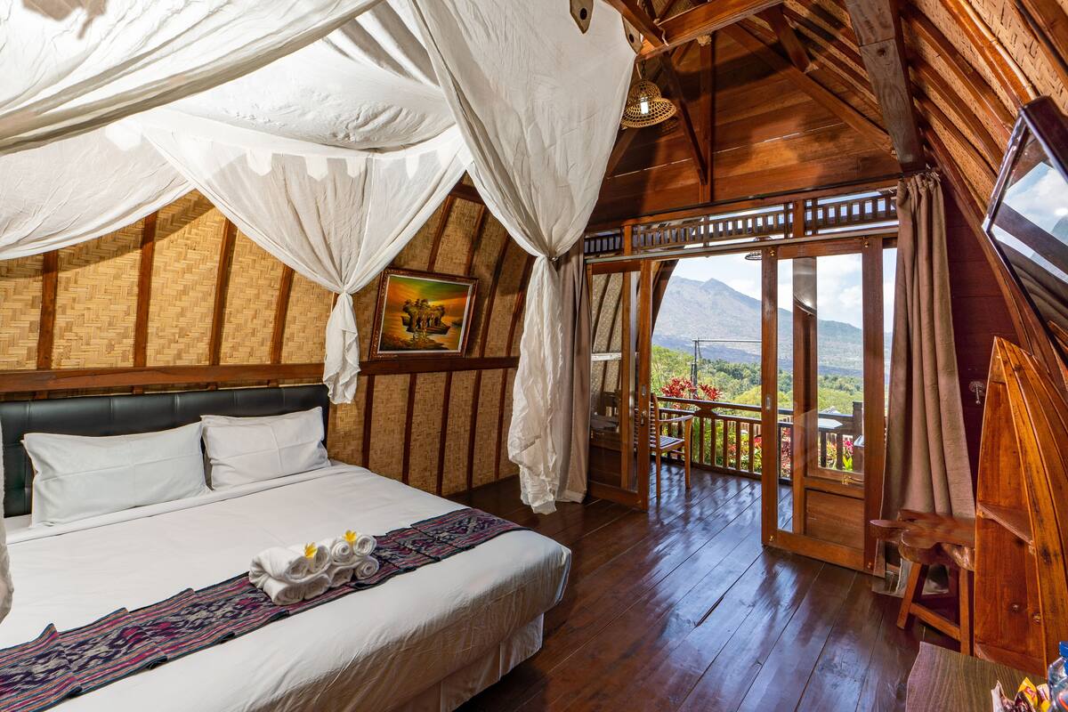 A bedroom with a large bed, wooden walls, a balcony with a view, and a painting on the wall.