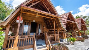 Eine Holzhütte mit geneigtem Dach, einer Veranda mit Holzgeländern und einem kleinen Sitzbereich im Freien.