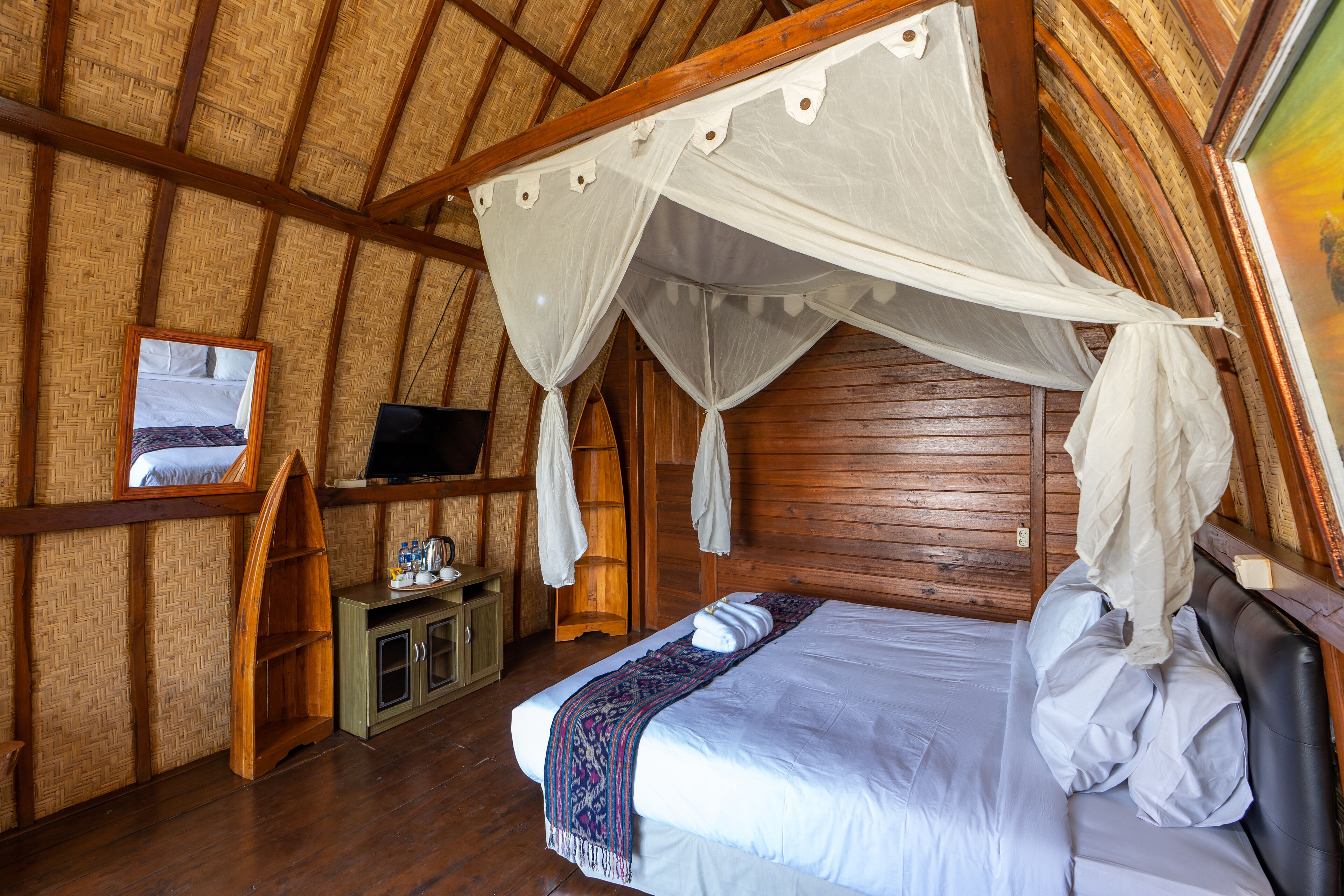 A room with a bed under a canopy, a television on a wooden cabinet, and a painting on the wall.