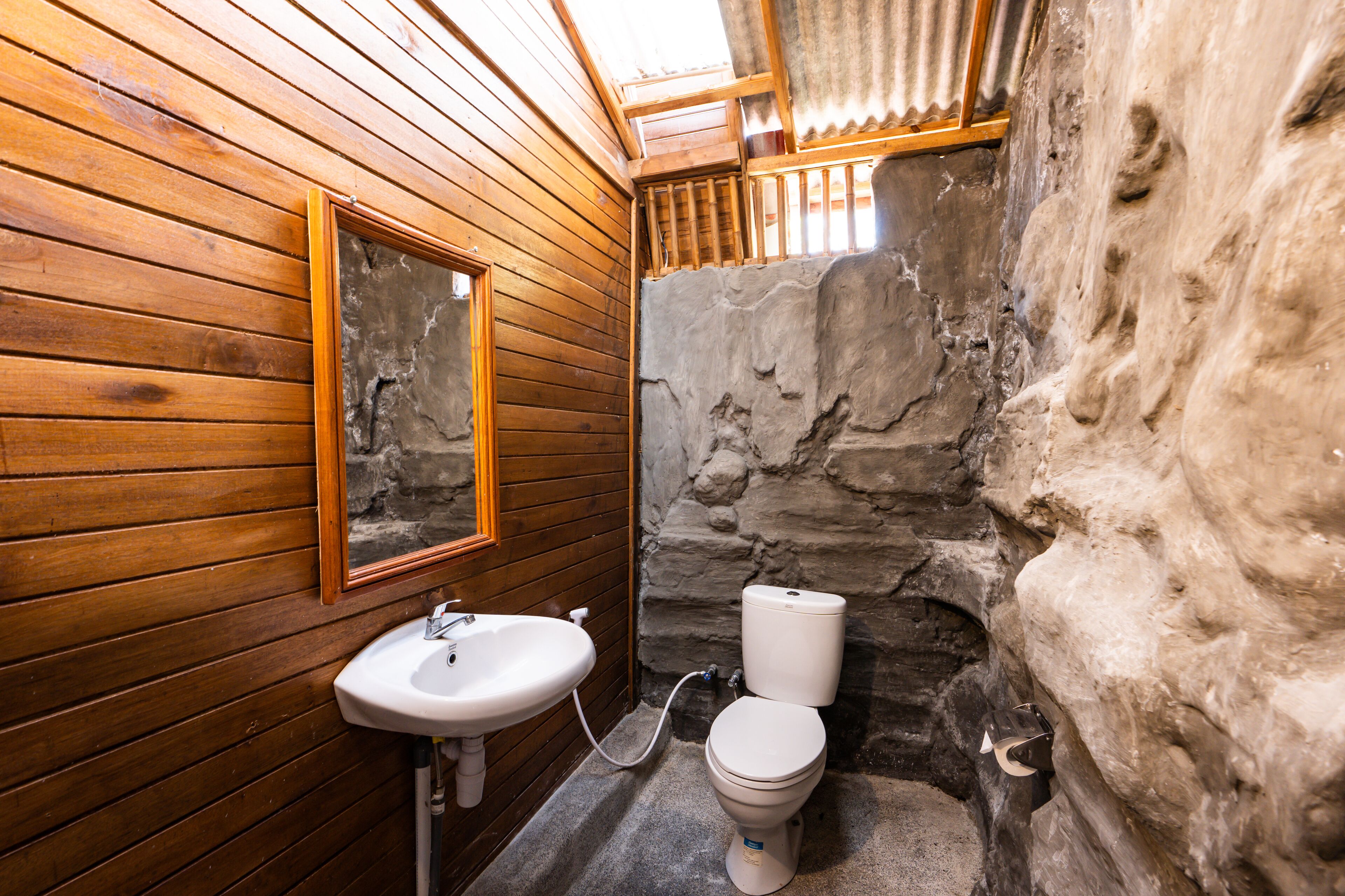 Ein Badezimmer mit Holzwänden, einer Steinwand, einem Waschbecken und einer Toilette.