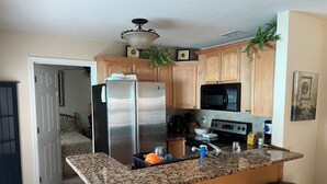 Una cocina con encimeras de granito, electrodomésticos de acero inoxidable, armarios de madera y una zona de bar con taburetes.