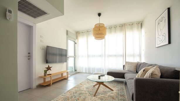 A modern living room with a sofa, a coffee table, a TV, and a patterned rug. - PORT CITY HAIFA - German Colony Luxury (Haifa)