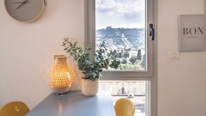 A dining area with a table, chairs, a clock, a window with a view, a plant, and a sign on the wall. - PORT CITY HAIFA - German Colony Luxury (Haifa)