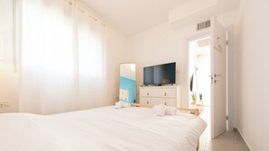 A hotel room with a large bed, a TV on a dresser, a mirror, and a door leading to another room. - PORT CITY HAIFA - German Colony Luxury (Haifa)