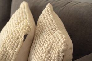 Een close-up van een textiel kussen in beige met een duidelijke naad en een donkerbruin lederen label.
