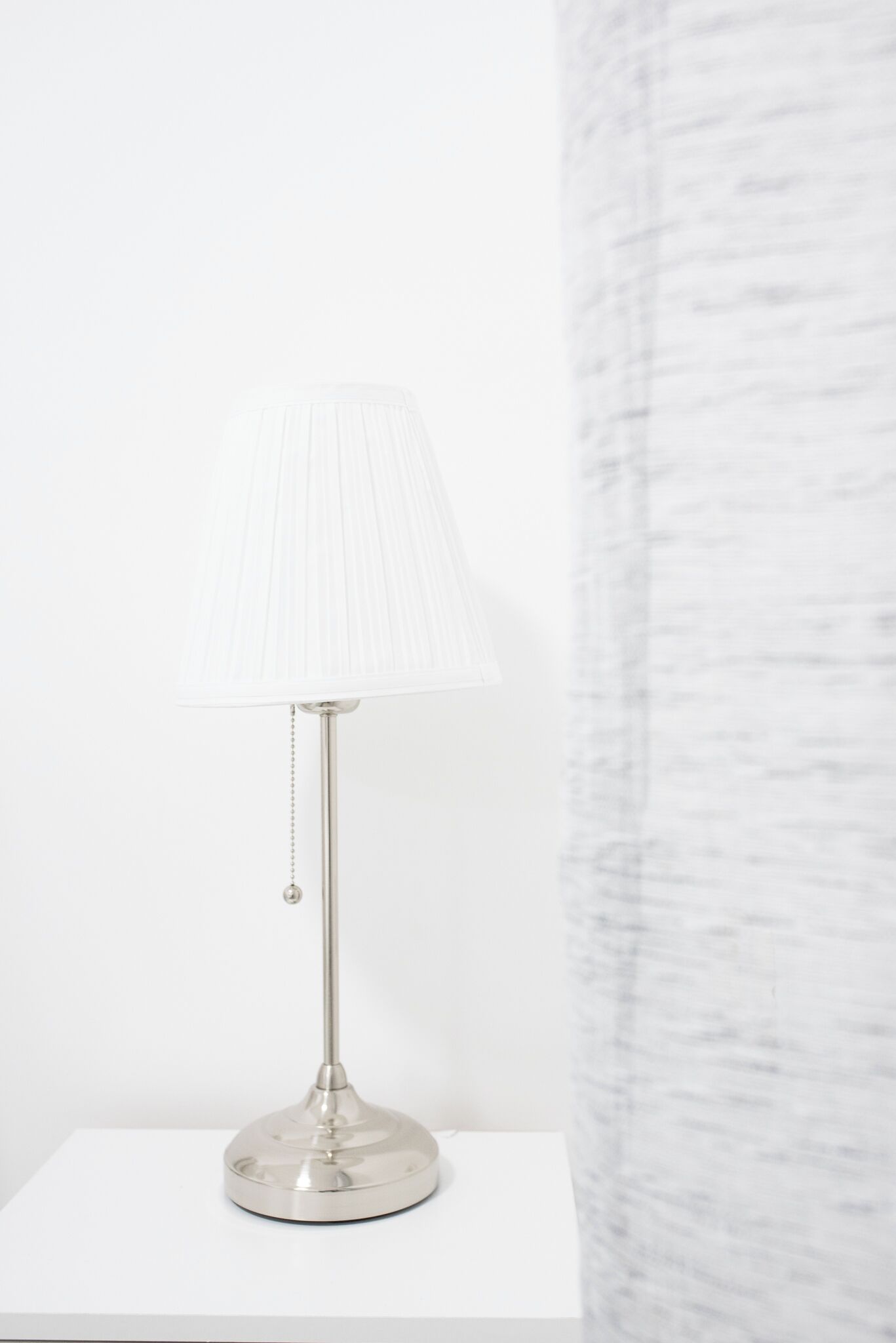 A modern table lamp with a white shade and a metallic base on a white surface.