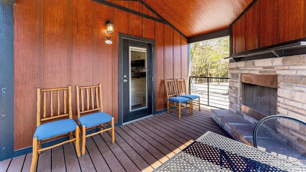 A wooden deck with two chairs and a table, a stone fireplace, and a door leading to a kitchen. - Indian Point Cabin 4 near Silver Dollar City, Table Rock Lake & Branson (Branson)
