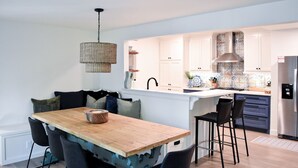 A modern kitchen with white cabinets, a stainless steel refrigerator, and a wooden dining table with black chairs. - Renovated Historic 5 Bedroom Home Close to OU Campus! (Norman)