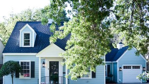 A two-story house with a dark roof, a front porch, and a garage. - Renovated Historic 5 Bedroom Home Close to OU Campus! (Norman)