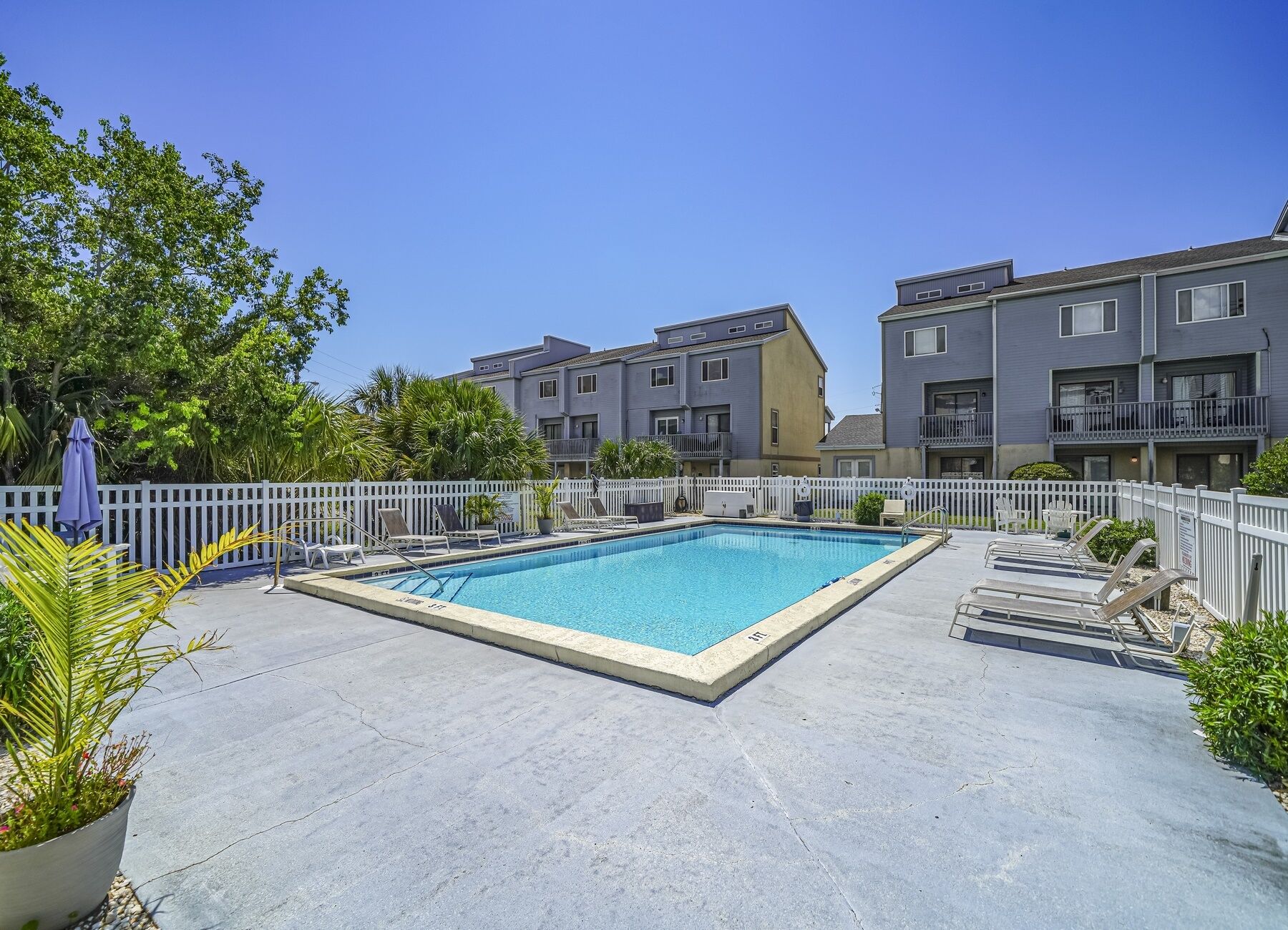 Una piscina rectangular con sillas de descanso y una cerca blanca.