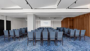 Une salle de conférence avec des rangées de chaises, un écran de projection et un mur en bois.