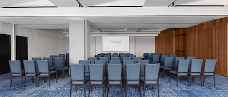 Une salle de conférence avec des rangées de chaises, un écran de projection et un mur en bois.