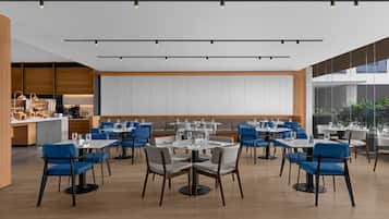 A modern restaurant with a central seating area, a bar, and a large window providing a view of the outdoors.
